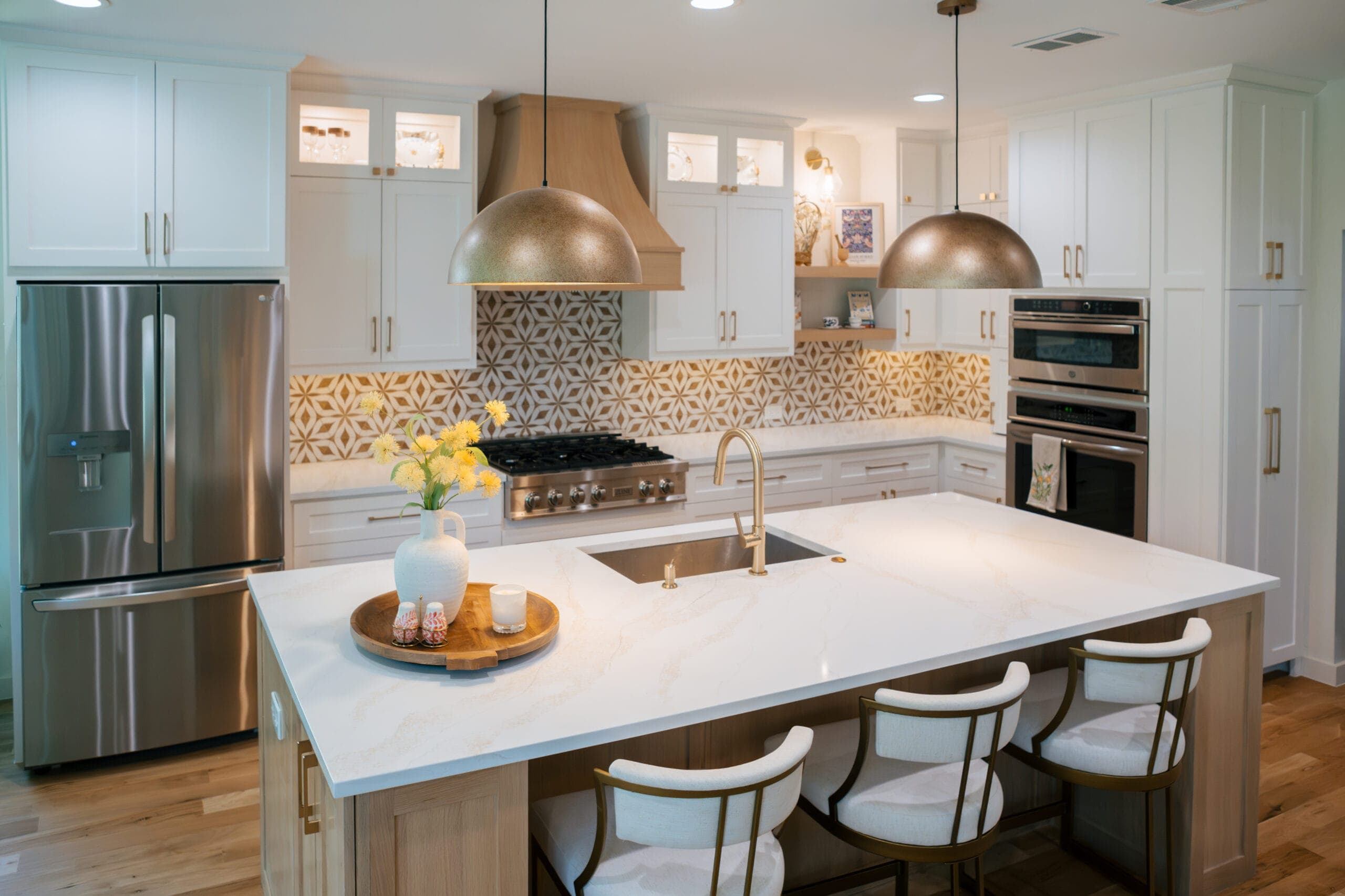 Quartz-topped island seating four, framed by white shaker cabinets and a white oak range hood